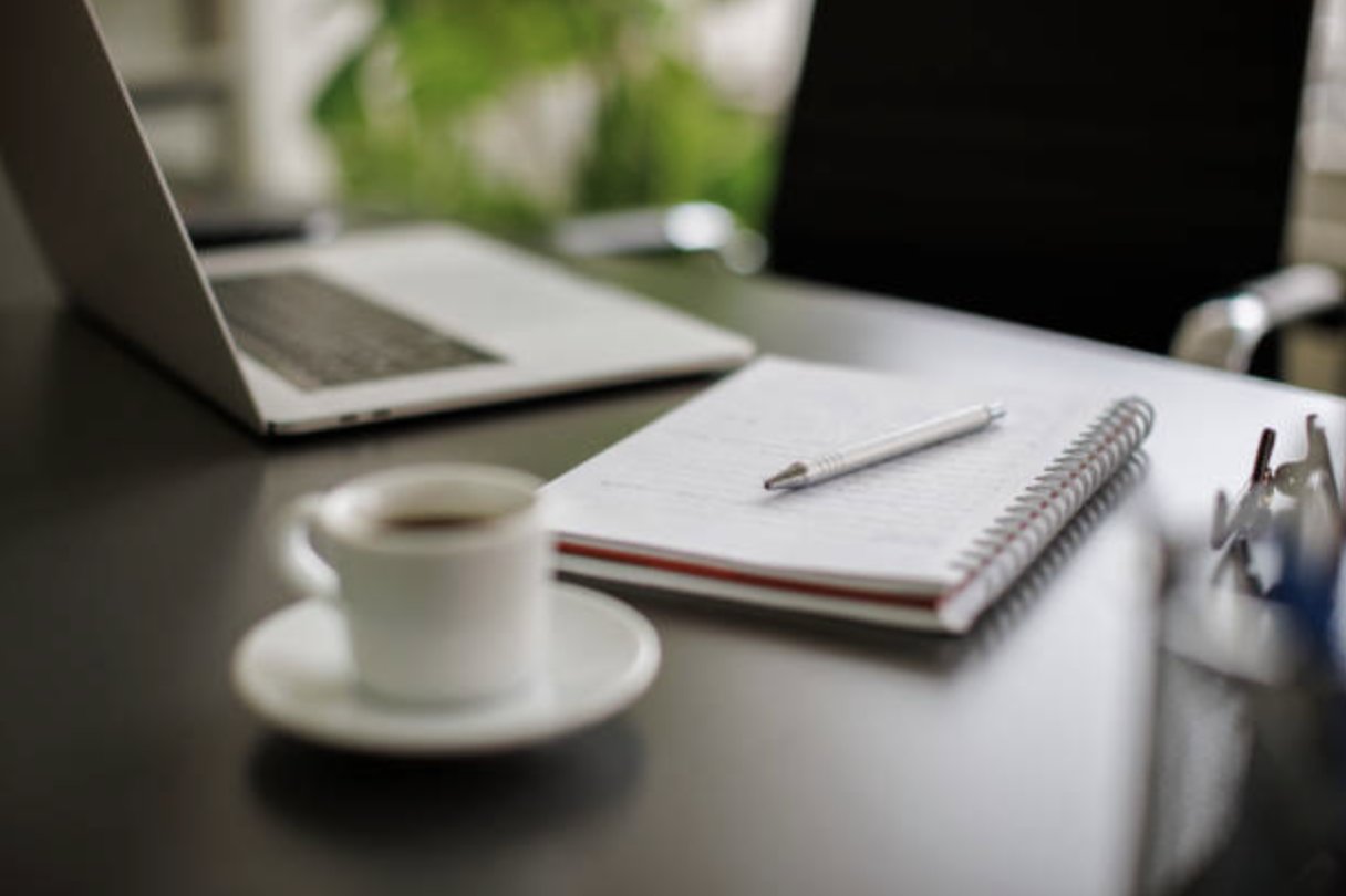 Coffee cup, notebook, and laptop on an office desk